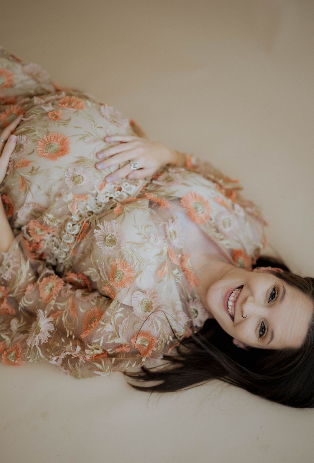 An artistic maternity photo showing a woman in a flowing floral dress laying down and smiling at the camera.
