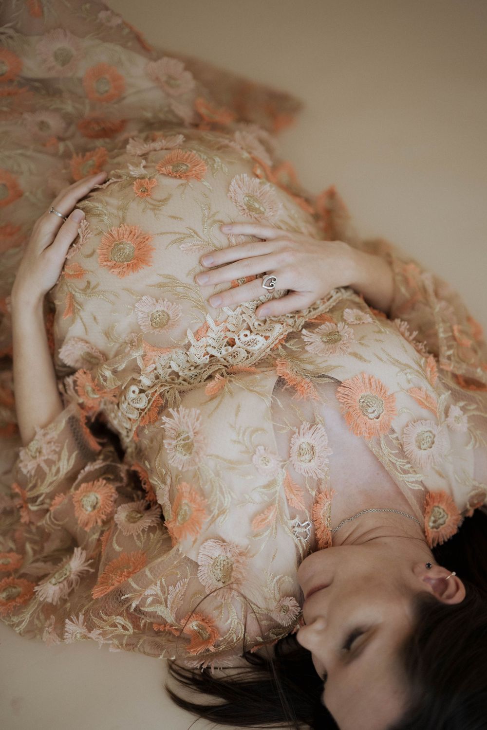 A dreamy portrait of someone lying down in a vintage floral dress with peach and cream tones in soft lighting.