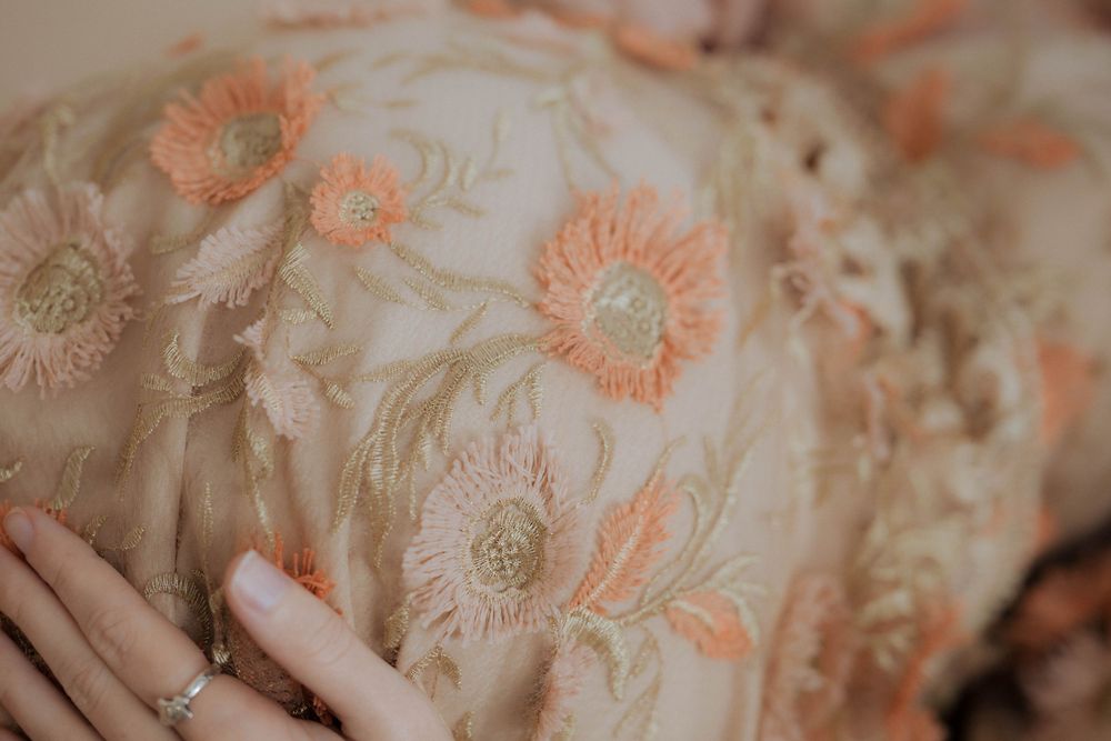 Delicate floral embroidery pattern in peach tones features daisies and lace details on light fabric.