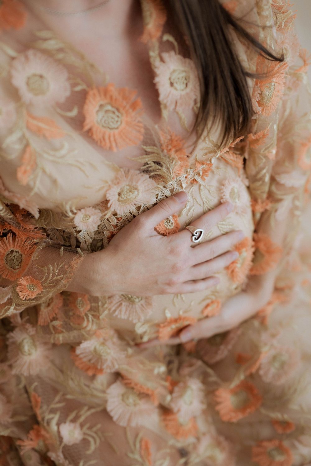 Close-up of hands with delicate rings resting on floral peach and cream fabric with embroidered flower pattern.