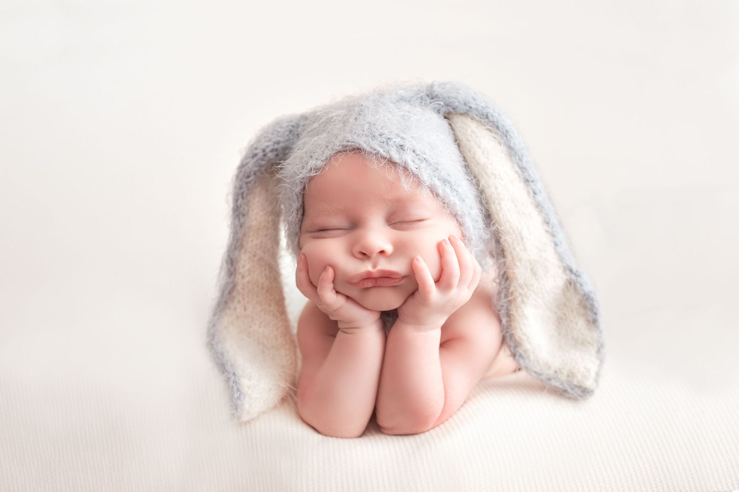 Sleeping newborn posed with bunny ears hat on white background.