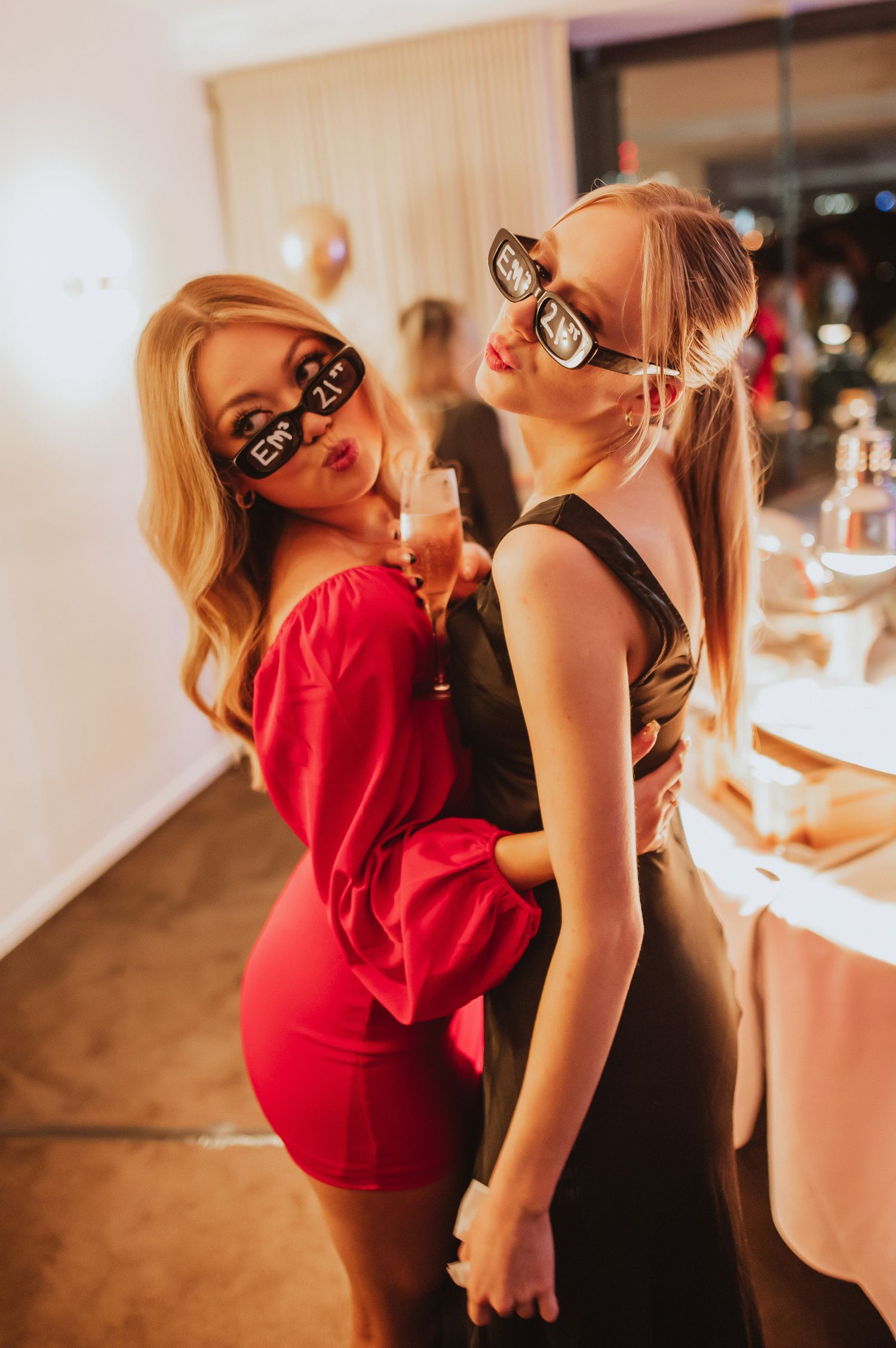 Two partygoers in festive attire posing playfully with matching novelty glasses.