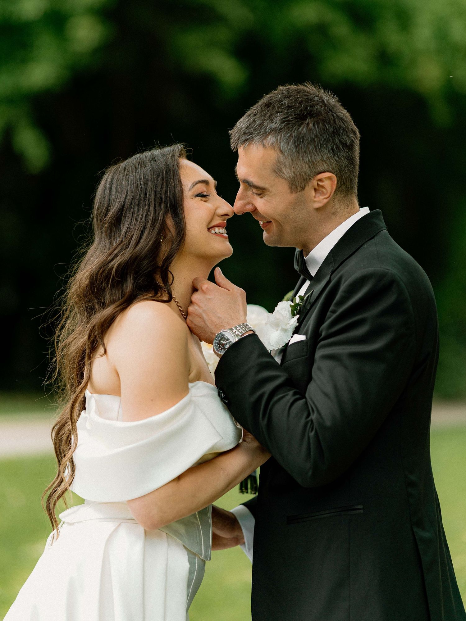 A couple shares a joyful moment under a black umbrella in formal wedding attire.