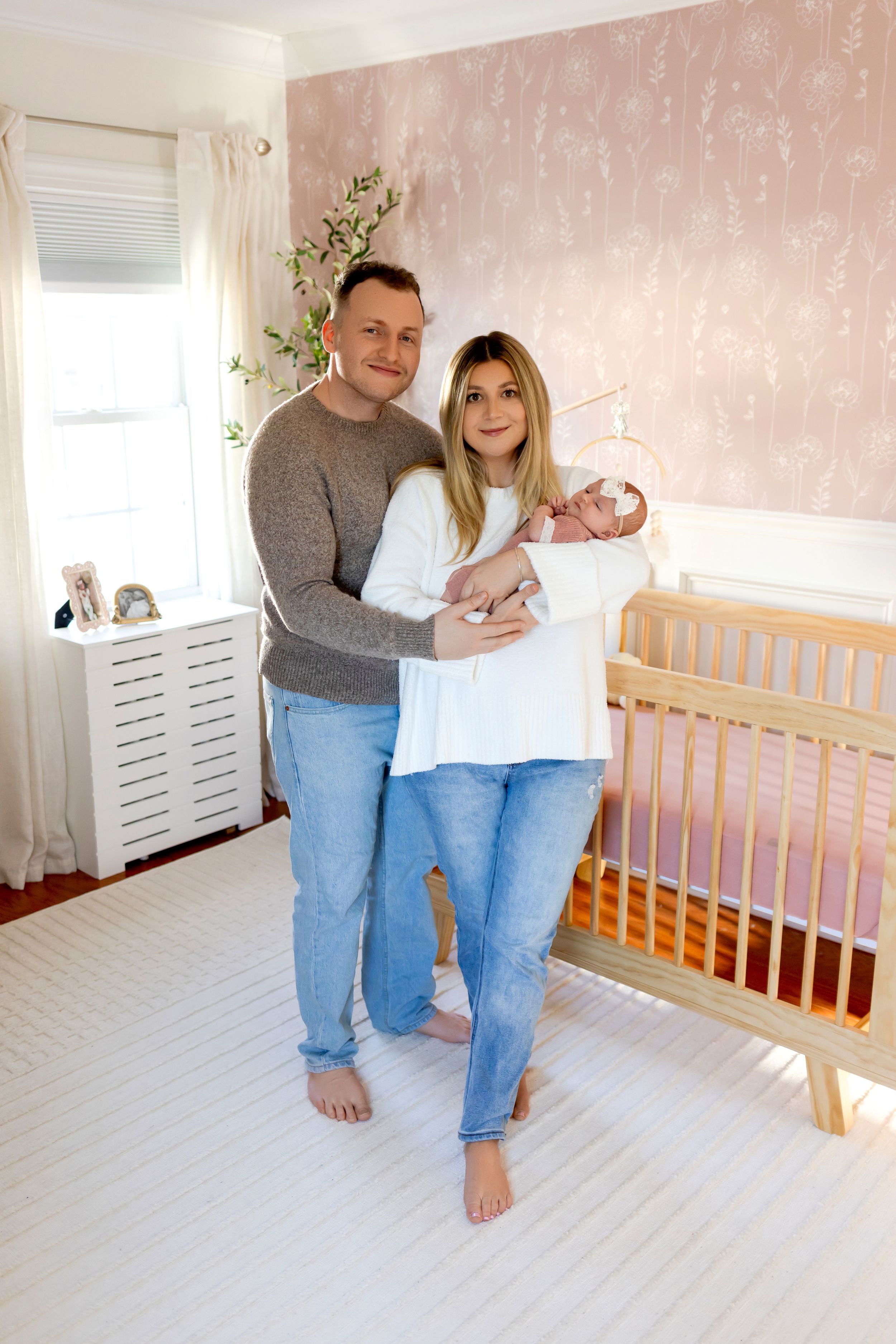 A couple poses with their newborn baby in a cozy nursery with pink walls.