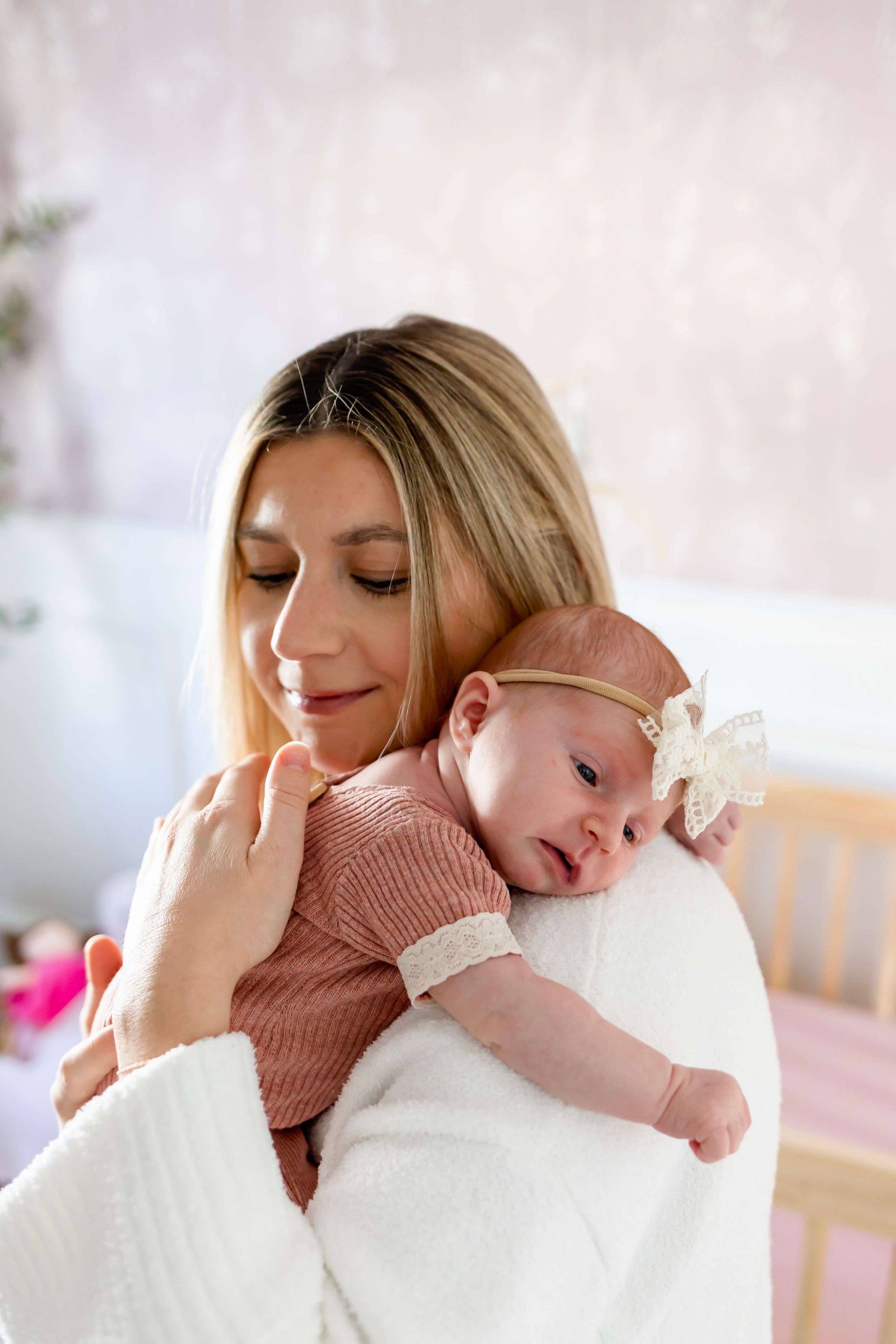 Mother in white sweater cradles sleeping baby wearing pink with white bow.