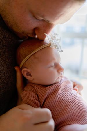 Close-up of gentle moment with sleeping newborn wearing lace headband.