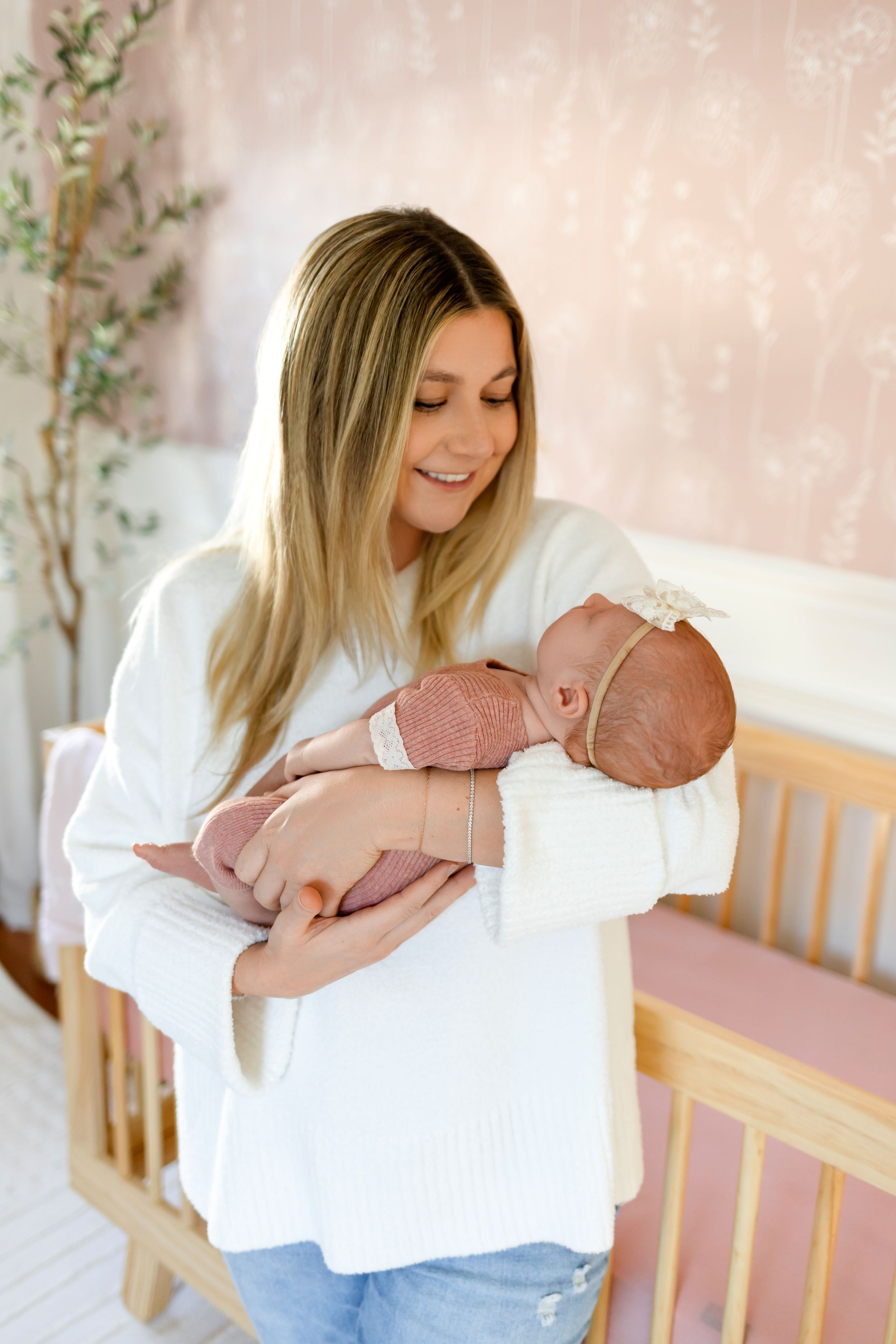 Mother in white top holds sleeping newborn baby wearing pink outfit.