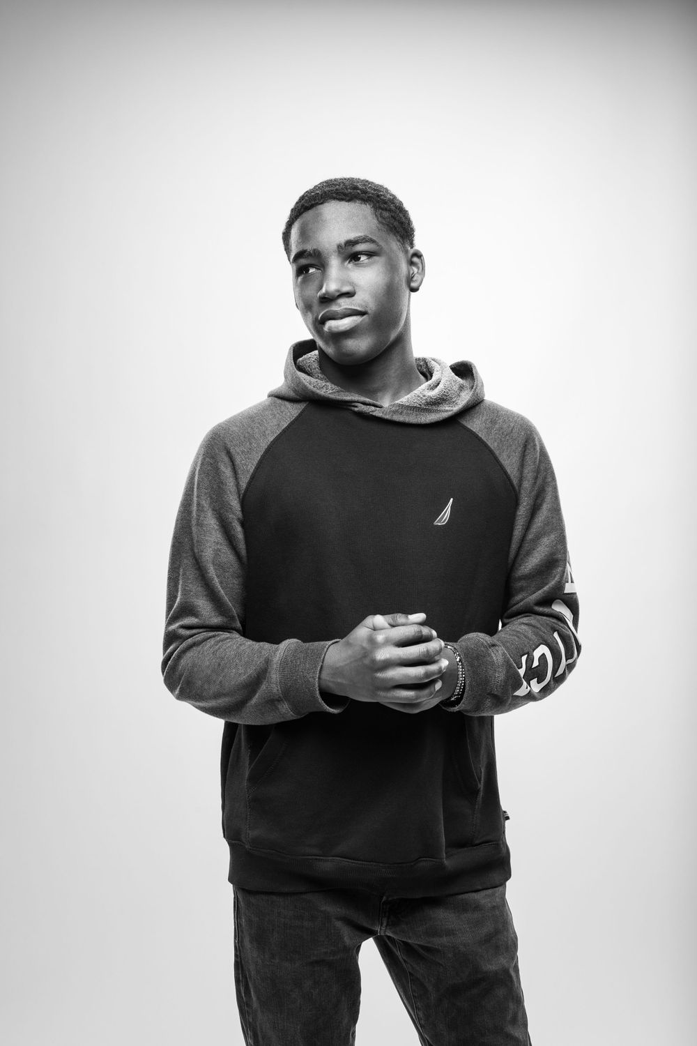 Young man poses in a casual black and grey hoodie against white background in black and white photography.