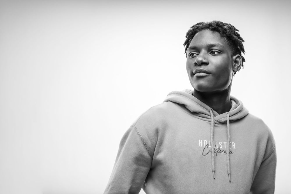 A black and white portrait of a person in a hoodie looking off to the side against a light background.