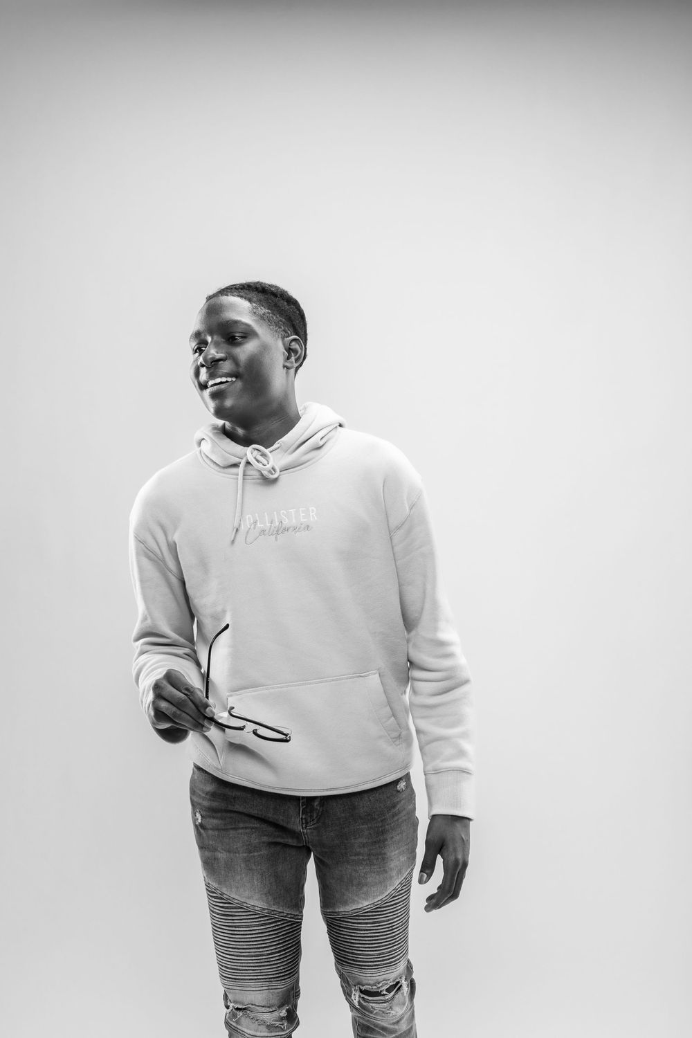 Person wearing white hoodie and distressed moto jeans poses casually against plain background in black and white photo.