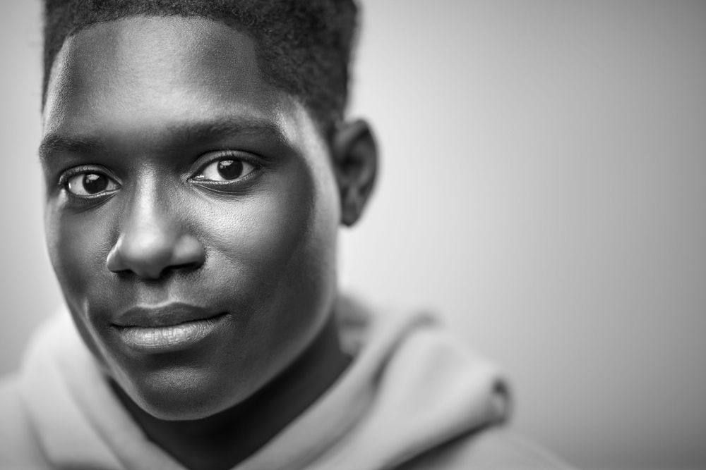 Black and white portrait of a young person in a hoodie looking at camera with a gentle smile.