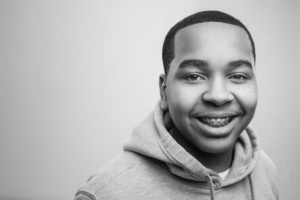 A black and white close-up portrait of a young person wearing a gray hoodie and smiling at the camera.