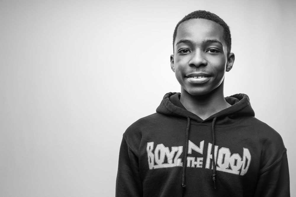 Black and white portrait of a young person wearing a dark hoodie with text against a plain background.