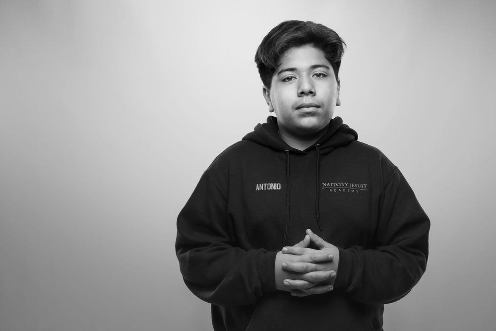 A person in a black hoodie standing against a gray background in a black and white photograph.