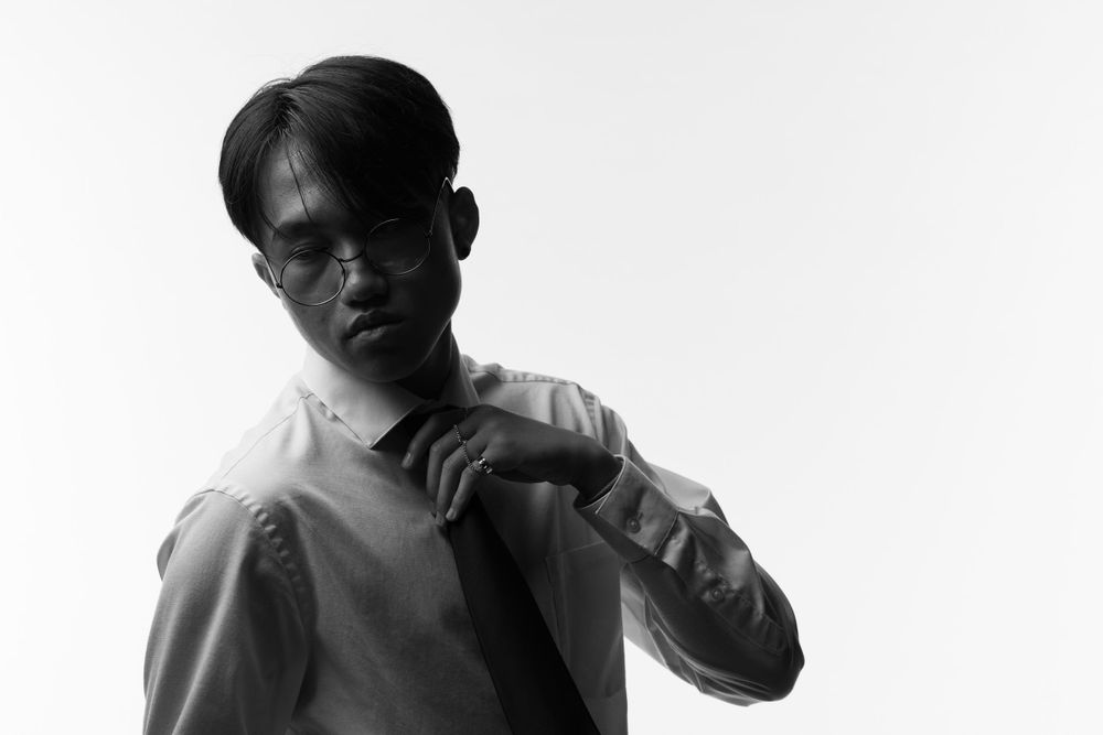 Black and white portrait of person in light colored clothing adjusting collar against white background.