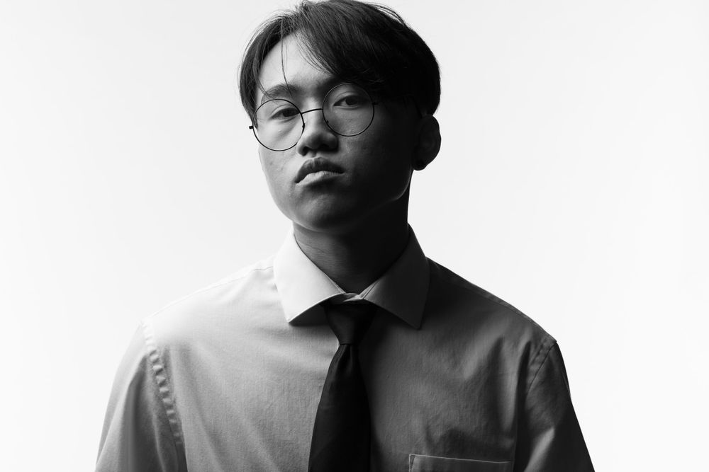Black and white portrait of someone wearing glasses, a dress shirt and tie with a minimalist background.