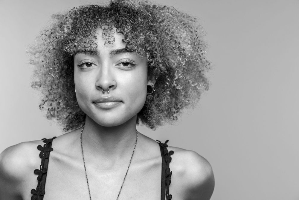 Black and white portrait of a person with natural curly hair against a light background wearing a dark top.