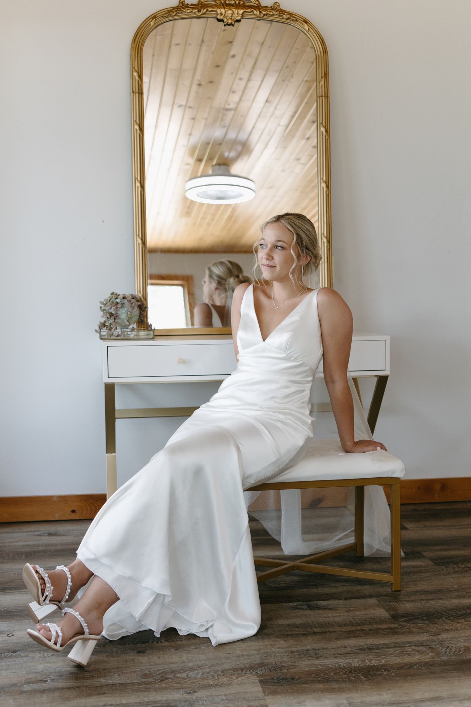 A bride in a classic white dress poses elegantly by a vintage gold mirror.