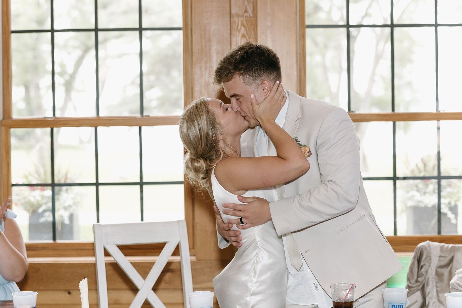 Romantic couple sharing their first kiss during a wedding ceremony near large windows.