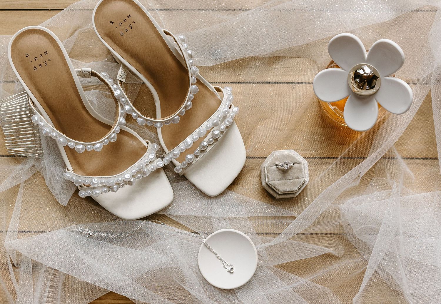 Wedding accessories including white heeled sandals and jewelry arranged on light fabric.