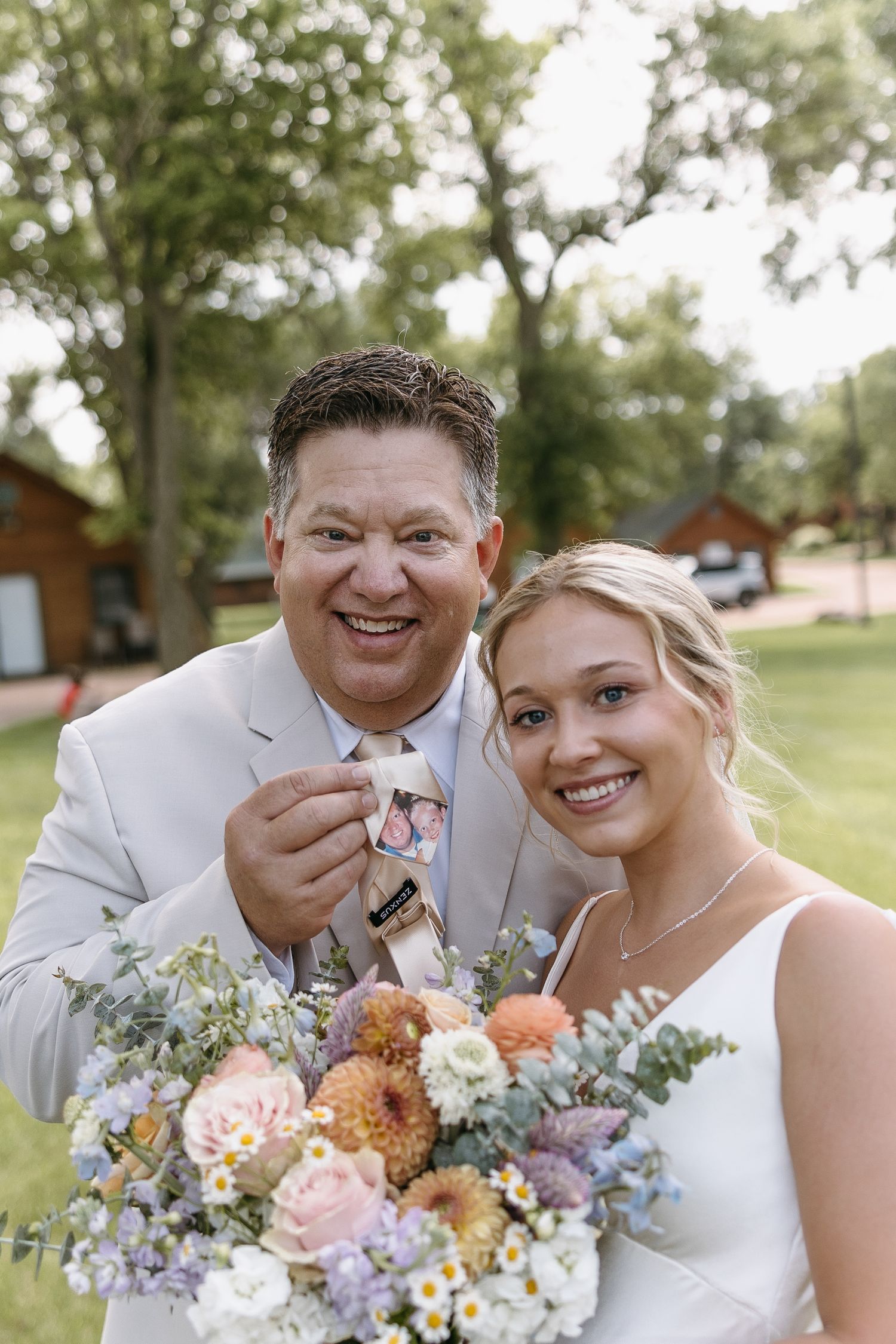 Wedding couple poses outdoors with vibrant floral bouquet featuring peach and purple blooms.