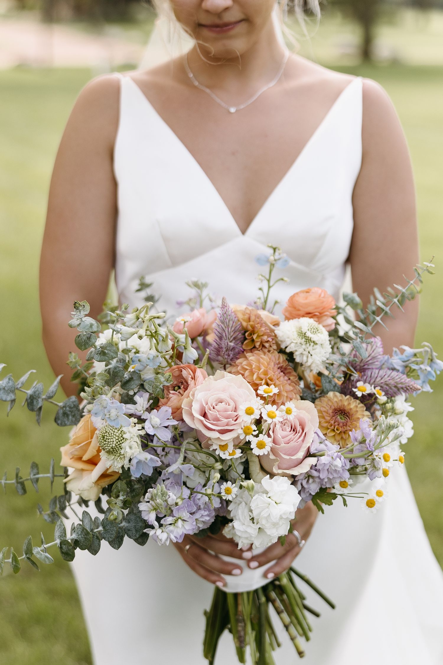 Close-up of bridal bouquet with pink roses, peach dahlias, and eucalyptus against white dress.
