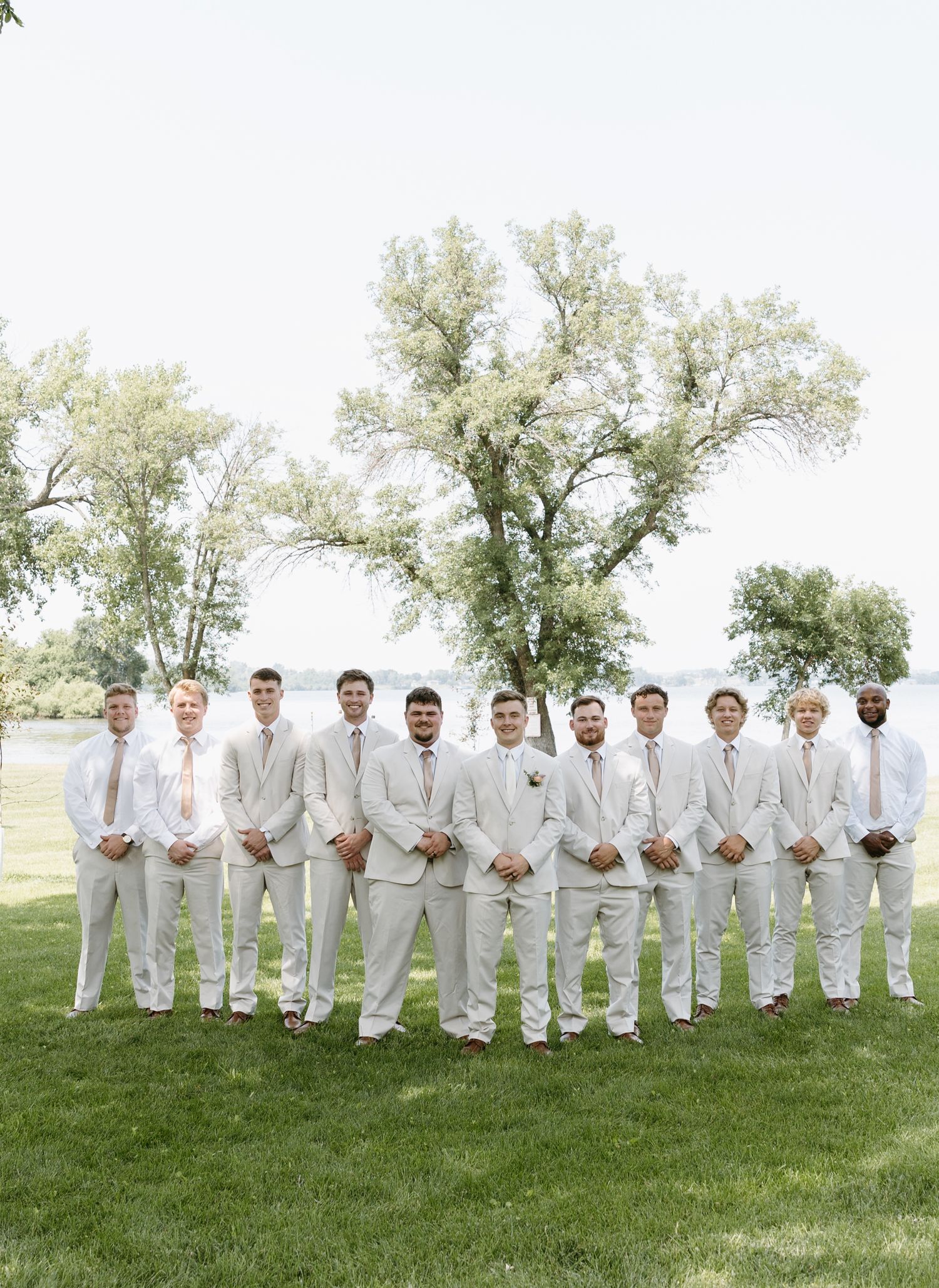Groomsmen in matching light suits line up on grass for formal wedding photo.