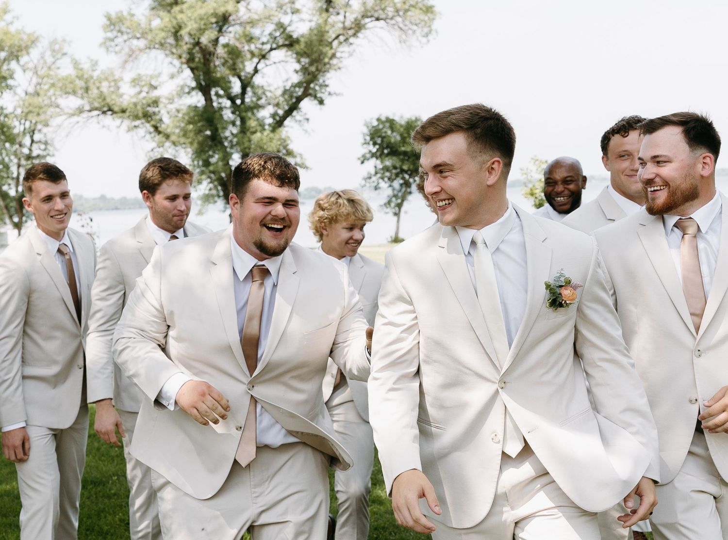 Candid moment of groomsmen laughing together in light suits outdoors.