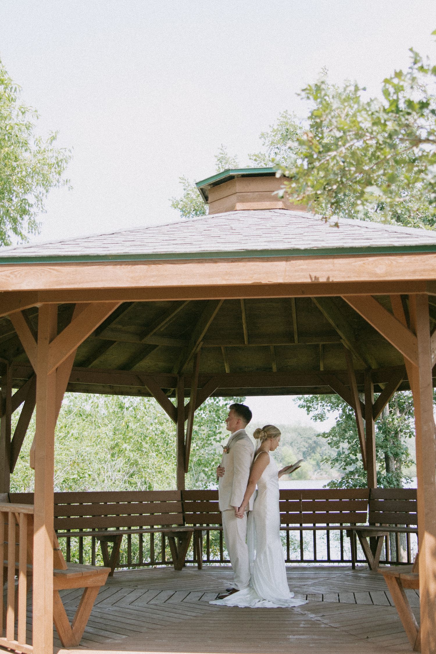 Couple poses back-to-back under wooden gazebo during wedding photoshoot.