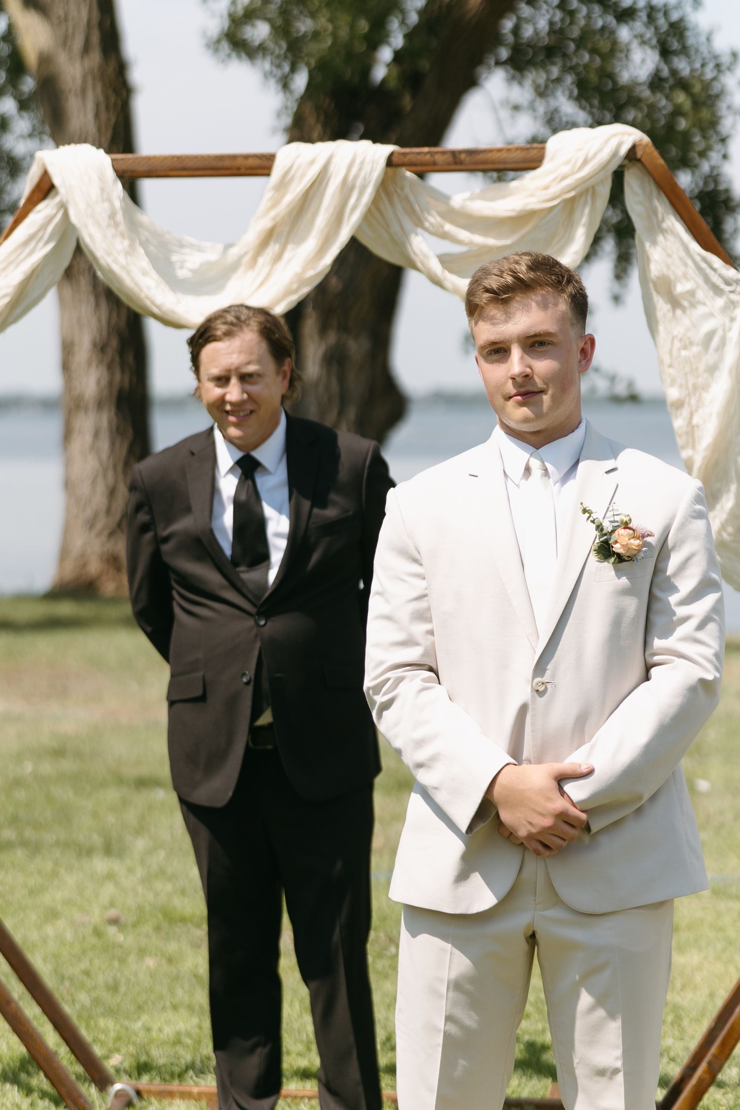 Wedding ceremony setup with white fabric arch and attendants standing outdoors.