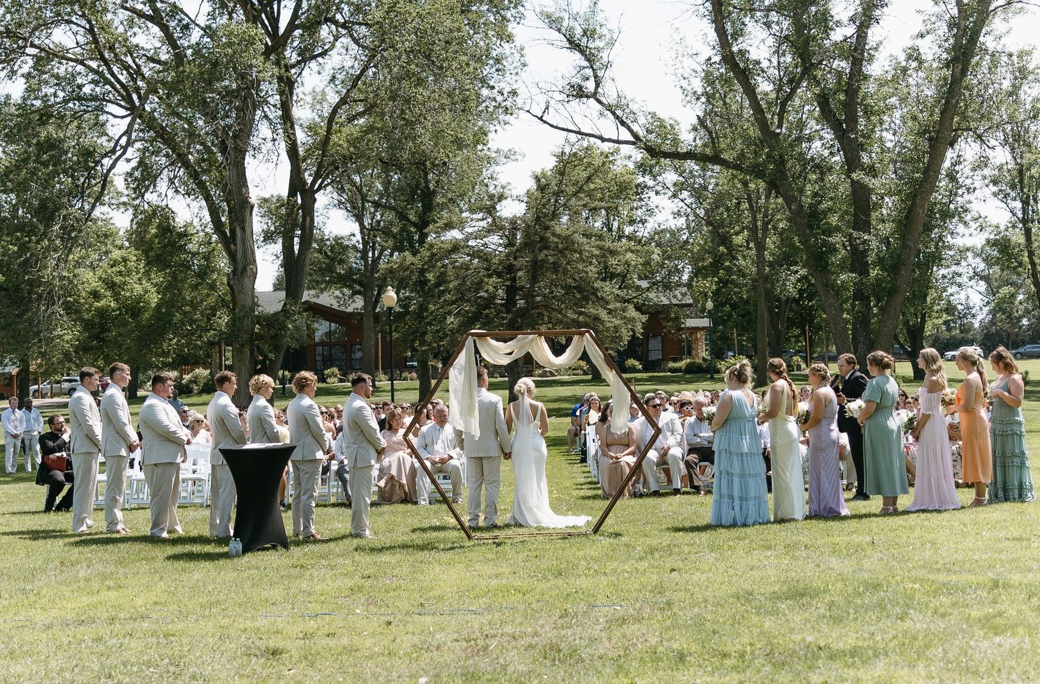 Large outdoor wedding ceremony with guests gathered in rows on a sunny lawn.