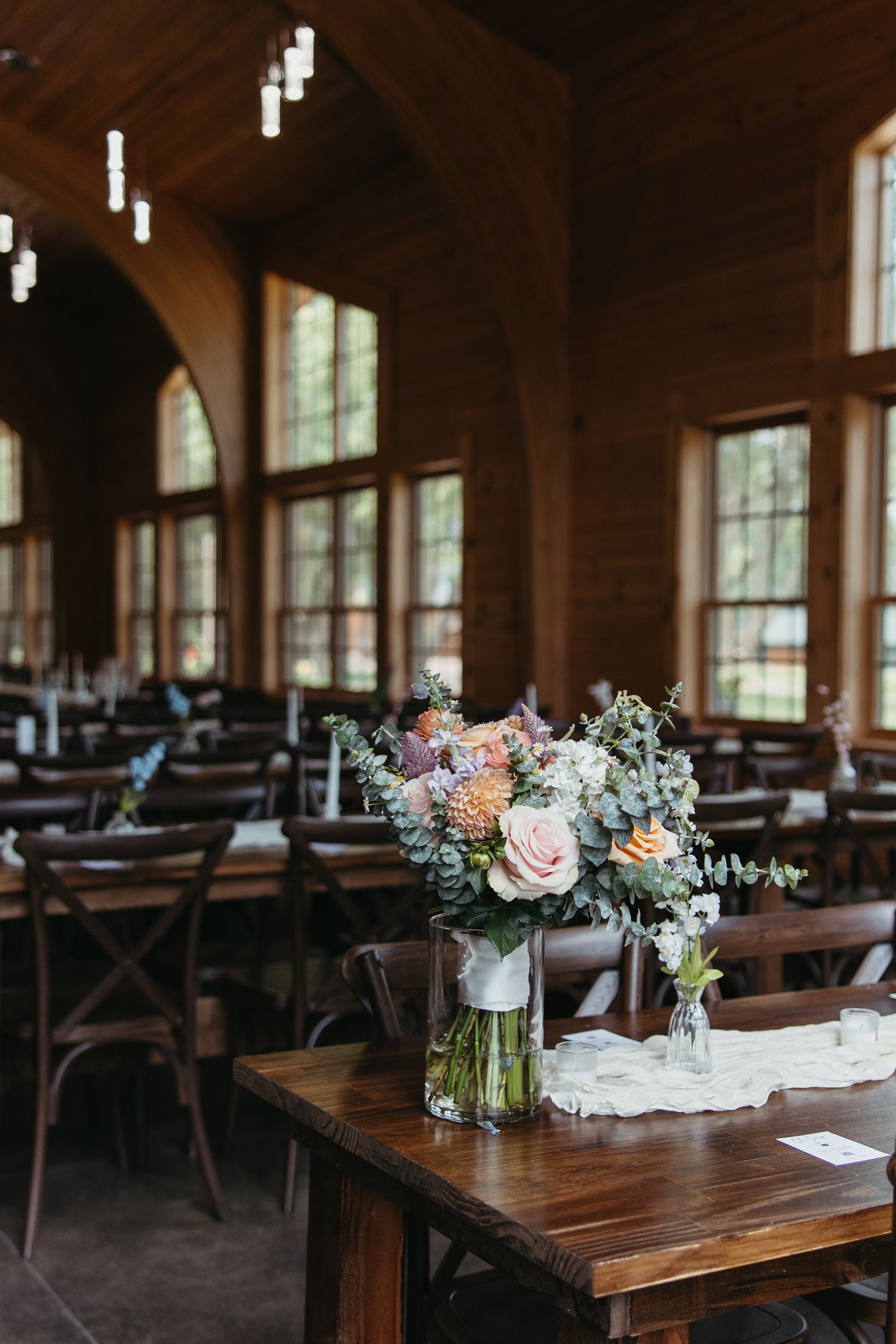 Rustic wedding reception venue with wooden tables decorated with soft floral centerpieces.