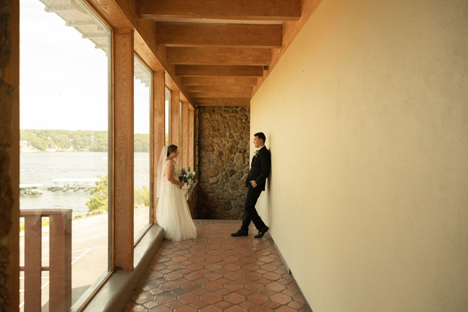 A romantic wedding portrait in a sunlit hallway with stone walls and wooden beams.