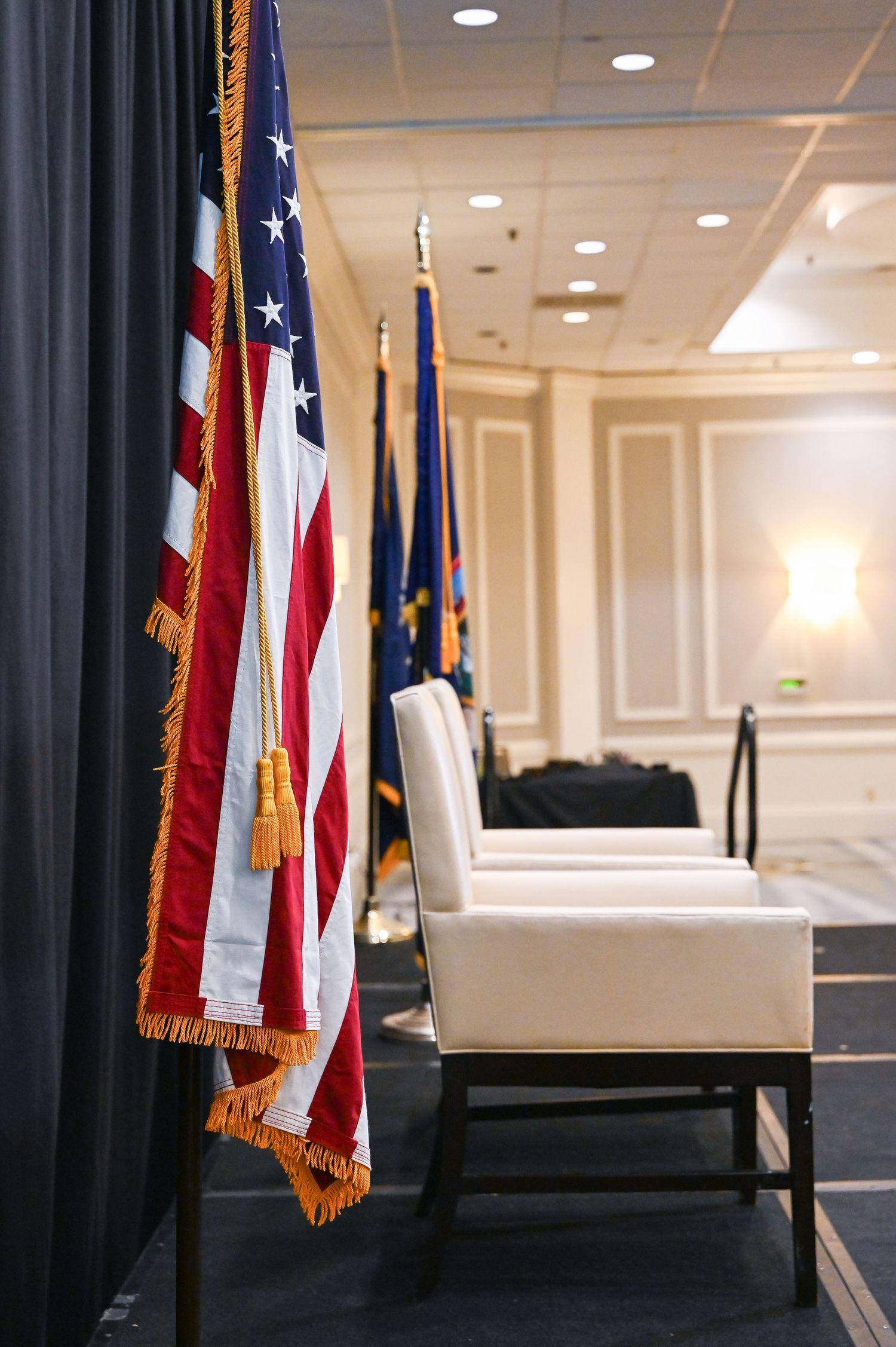 American flag with gold fringe stands prominently in an elegant conference room.