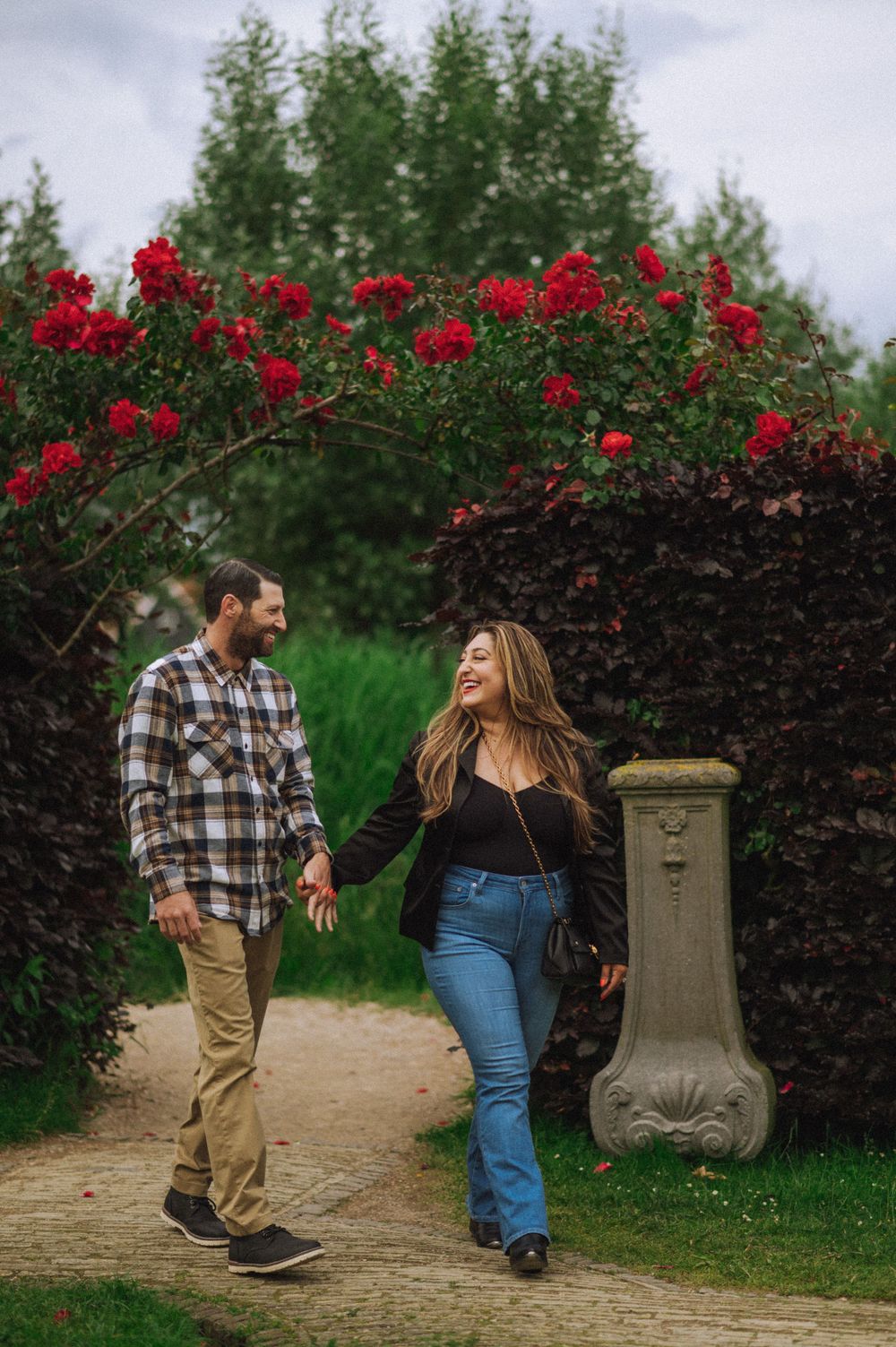 Couple walking along a garden path with blooming red roses and greenery.