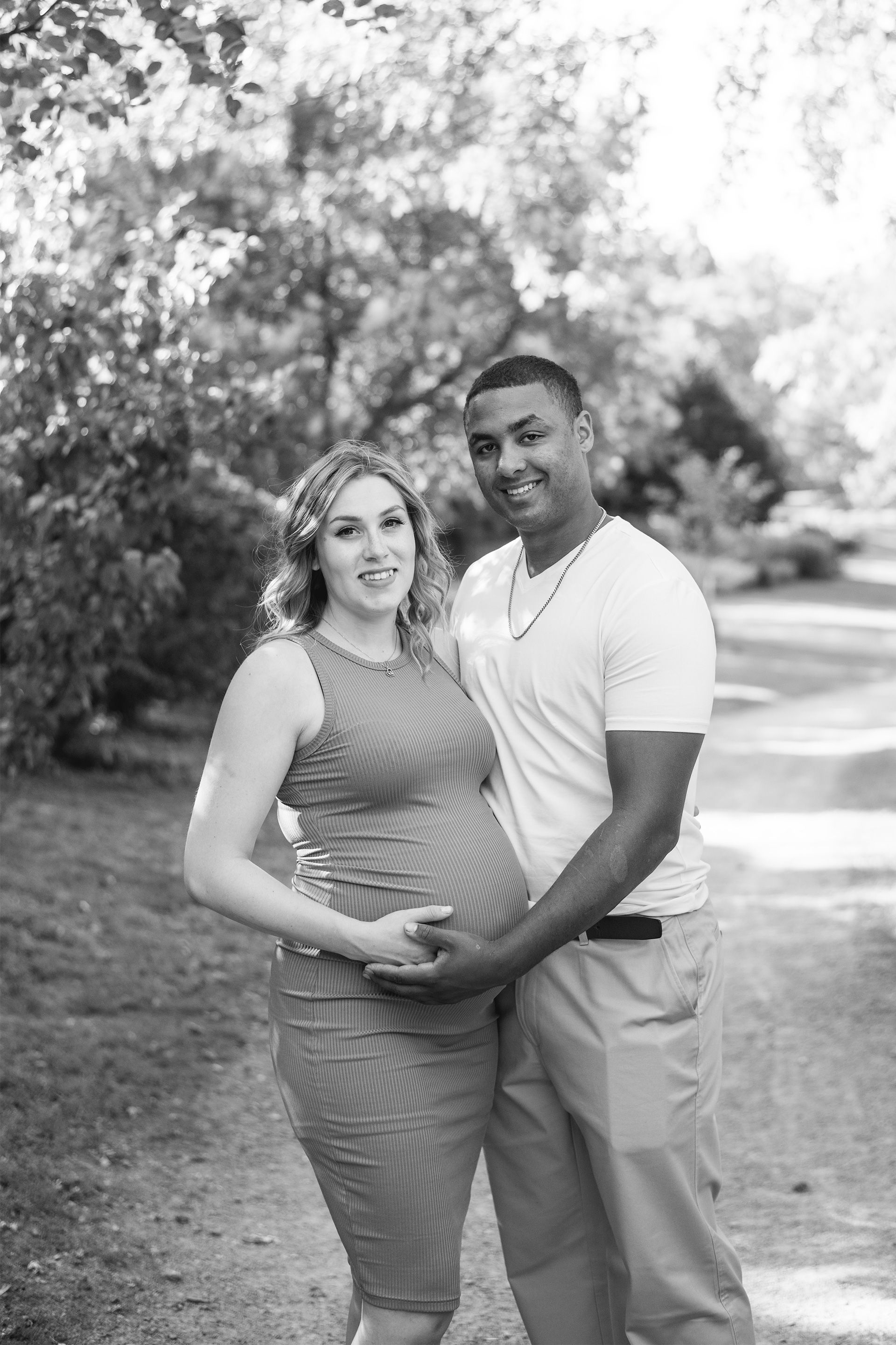 Black and white maternity photo of couple posing on outdoor path.