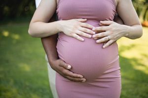 Close-up of hands cradling a pregnant belly in a pink ribbed dress.