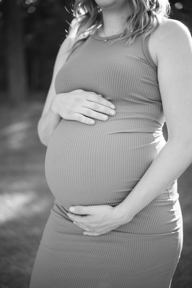 Black and white close-up of pregnant woman's hands resting on her belly.