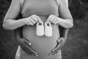 Black and white photo of hands holding tiny baby shoes against maternity dress.