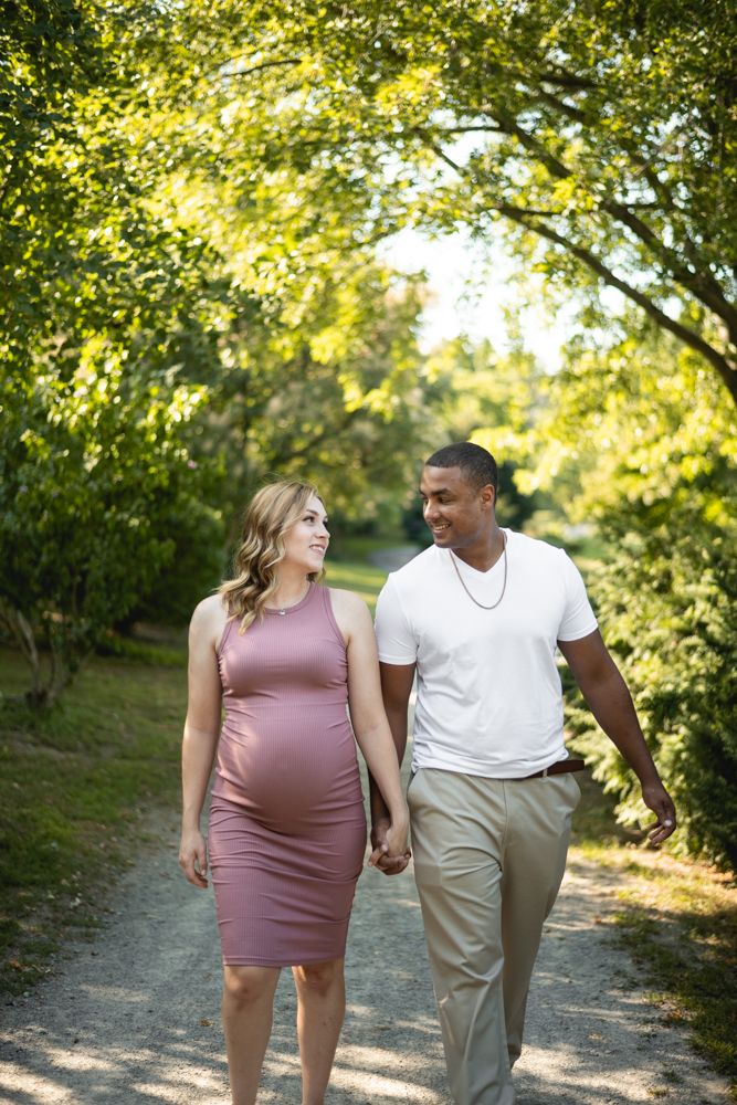 Couple walks hand in hand on nature path surrounded by lush green trees.