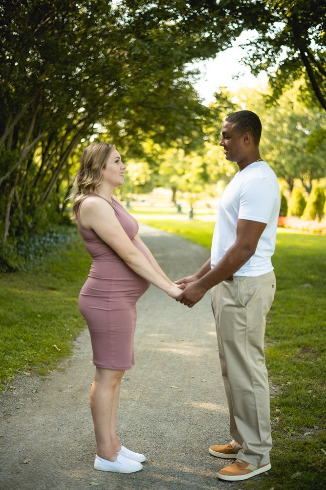 Happy couple holds hands while standing on a garden path during maternity photoshoot.
