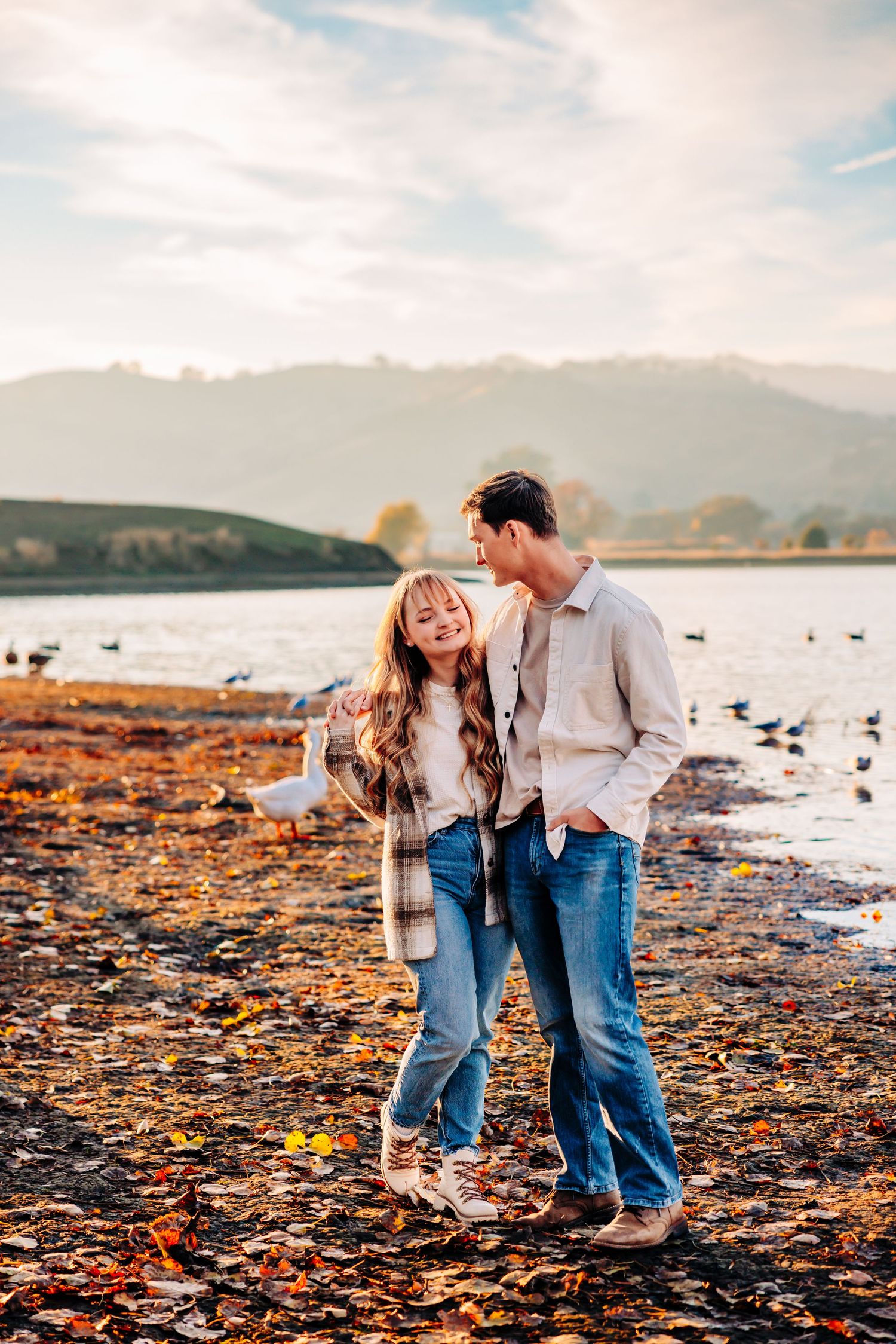 Couple laughing together on rocky shoreline during sunset.