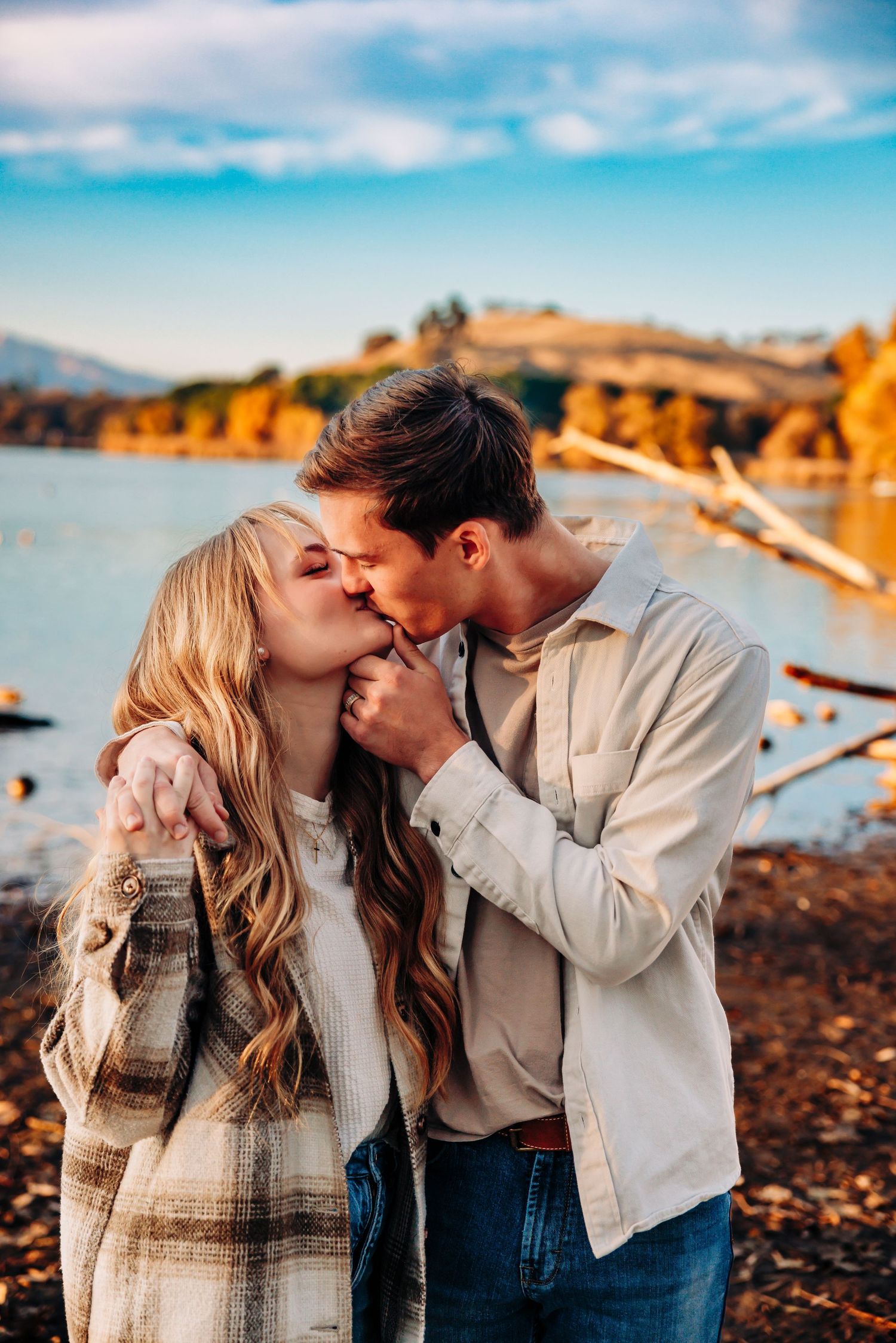 Romantic couple sharing intimate moment on lakeside beach at sunset.