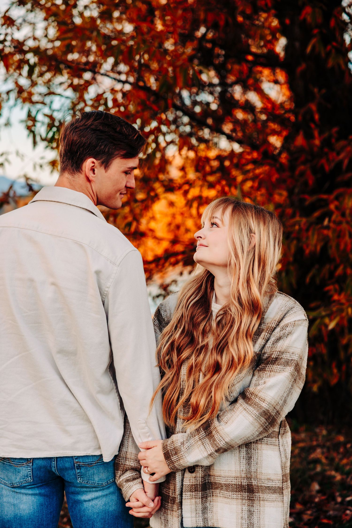 Romantic autumn moment between couple under vibrant orange fall foliage.