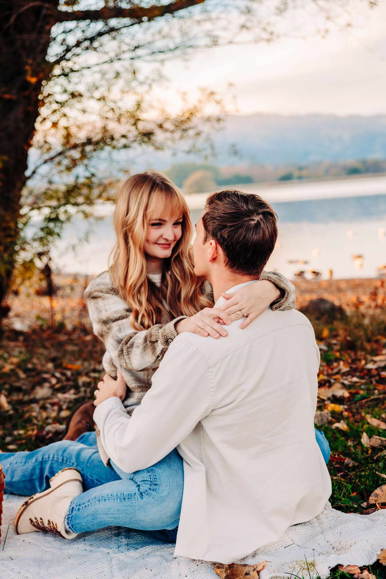 Intimate lakeside moment on blanket surrounded by fallen autumn leaves.