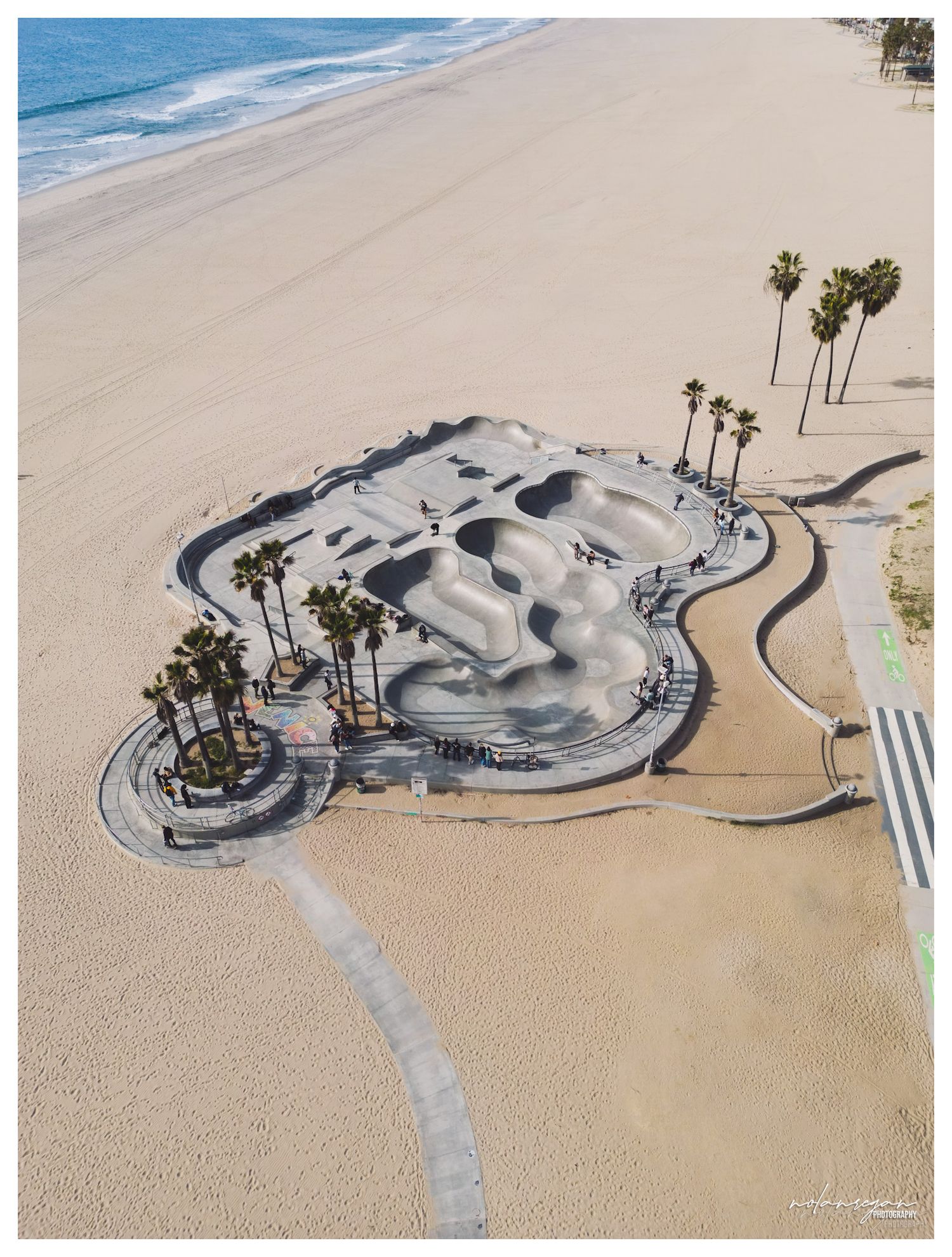 Aerial view of concrete skate park on sandy beach with palm trees.