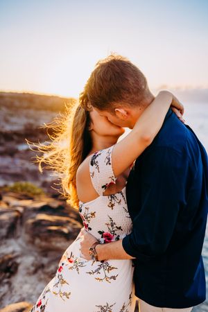 A couple embraces on a scenic cliff overlooking the ocean during golden hour in kaanapali maui for couples photography session sunrise