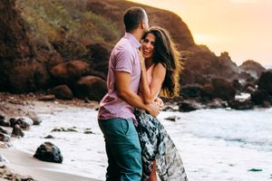 maui hawaii proposal photography. Romantic couple embracing on a rocky beach at sunset with waves crashing in the background.