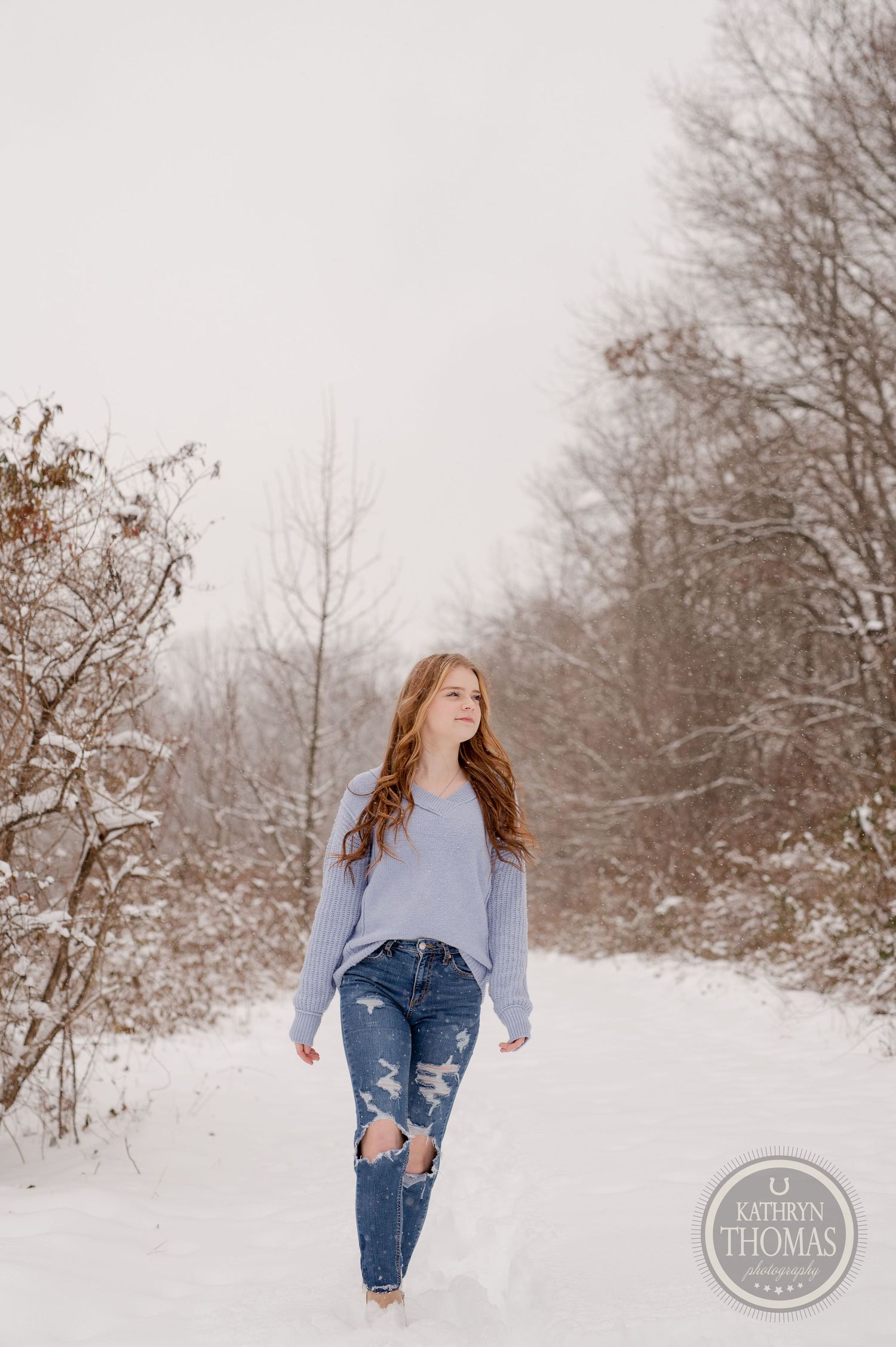 Fashion portrait in distressed jeans and oversized sweater on a snowy winter trail.