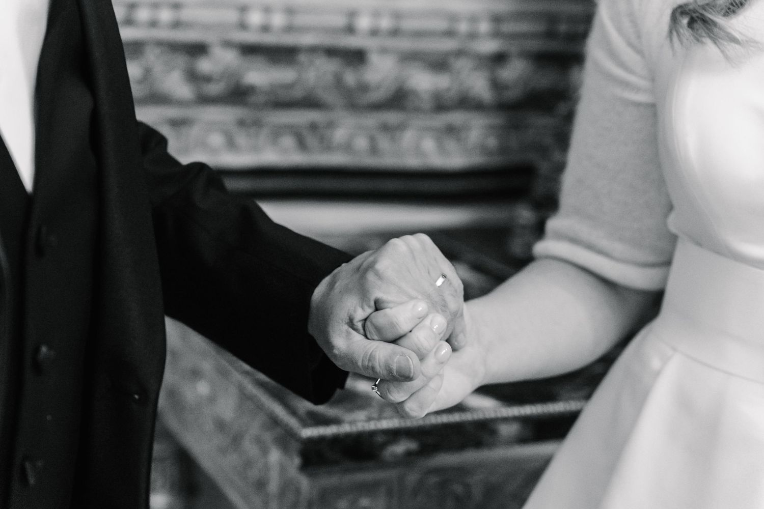 A black and white photo of newlyweds holding hands showing their wedding rings.